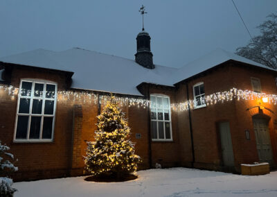 A picture of Dumbleton Village Hall in the snow with a Christmas tree in front